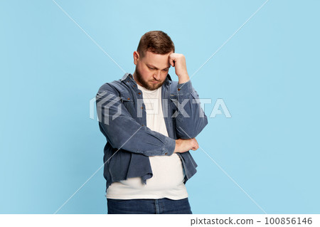 One pensive man standing with folded hands and thinking with sad facial expression over blue background 100856146