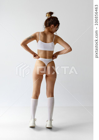 Full-length back view image young girl with slim, fit body posing in underwear, high socks and sneakers against grey studio background. Full-length back view image young girl with slim, fit body posing in underwear, high socks and sneakers against grey studio background. 100856463