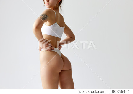Cropped image of fit female body, buttocks against grey studio background. Model posing in underwear Cropped image of fit female body, buttocks against grey studio background. Model posing in underwear 100856465
