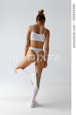 Full-length back view image young girl with slim, fit body posing in underwear, high socks and sneakers against grey studio background. Full-length back view image young girl with slim, fit body posing in underwear, high socks and sneakers against grey studio background. 100856466