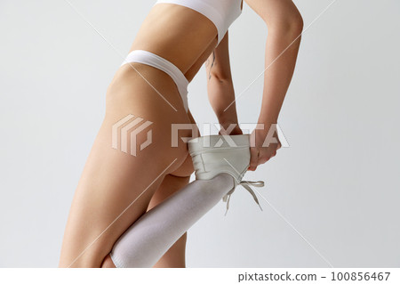 Cropped image of fit female body, buttocks against grey studio background. Model posing in underwear and sneakers. Cropped image of fit female body, buttocks against grey studio background. Model posing in underwear and sneakers. 100856467