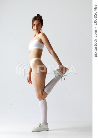Full-length portrait of young girl with slim, fit body posing in underwear, high socks and sneakers against grey studio background. Full-length portrait of young girl with slim, fit body posing in underwear, high socks and sneakers against grey studio background. 100856468