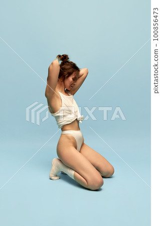Portrait of young girl with slim body, in underwear and socks posing against blue studio background. Body-positivity 100856473