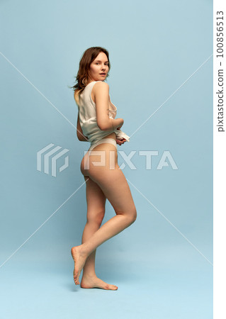 Full-length image of slim, beautiful, young girl in comfortable homewear posing against blue studio background. Anti-cellulite care Full-length image of slim, beautiful, young girl in comfortable homewear posing against blue studio background. Anti-cellulite care 100856513