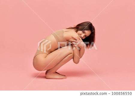 Tender femininity. Portrait of attractive, cute, young girl in beige underwear posing against pink studio background. Tender femininity. Portrait of attractive, cute, young girl in beige underwear posing against pink studio background. 100856550