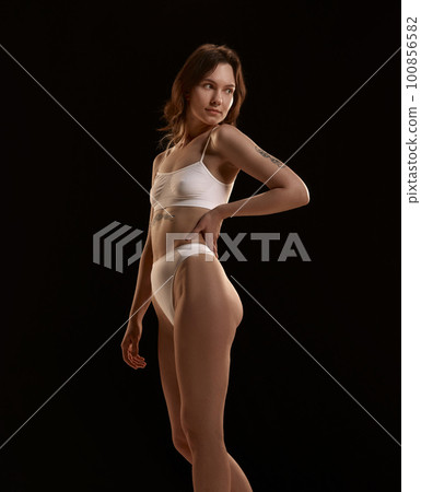 Attractive, young girl with slim, fit, healthy body posing in underwear against black studio background. Well-being and self-care 100856582