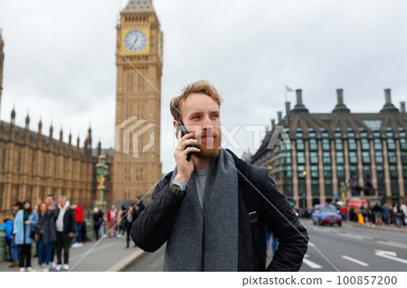 Bearded man is talking on the phone while standing on the street of London against the background of Big Ben Bearded man is talking on the phone while standing on the street of London against the background of Big Ben 100857200