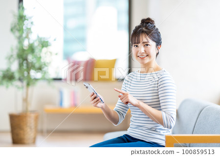 Young woman looking at her smartphone in the living room Young woman looking at her smartphone in the living room 100859513