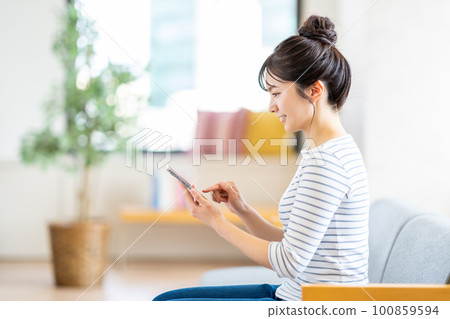 A young woman looking at her smartphone in the living room. A young woman looking at her smartphone in the living room. 100859594