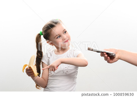 little girl shows with finger that she does not want chocolate and that she chooses banana, white background and copy space. little girl shows with finger that she does not want chocolate and that she chooses banana, white background and copy space. 100859630
