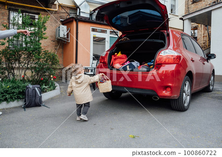 Family road trip where toddler little girl is helping to load up the trunk with suitcases and backpacks. Little girl help and put bags into the car trunk 100860722