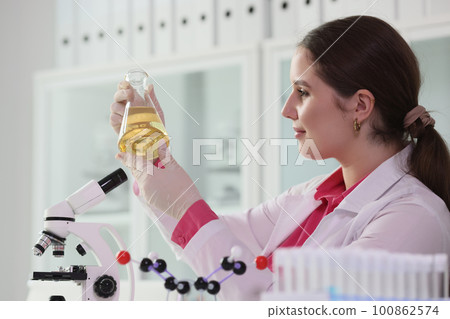 Brunette woman holds flask with yellow oil in laboratory Brunette woman holds flask with yellow oil in laboratory 100862574