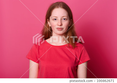 Half lengh portrait of young student female looks with calm facial expression at camera, wearing red casual t shirt, has long straight brown hair and beautiful blue eyes, isolated over pink background Half lengh portrait of young student female looks with calm facial expression at camera, wearing red casual t shirt, has long straight brown hair and beautiful blue eyes, isolated over pink background 100862671