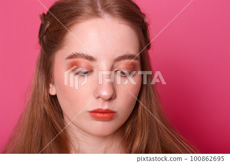 Studio portrait of beautiful young woman, has hair with red shade. Pretty model girl with perfect fresh clean skin. Attractive female with bright makeup, looks down. Beauty and skin care concept. Studio portrait of beautiful young woman, has hair with red shade. Pretty model girl with perfect fresh clean skin. Attractive female with bright makeup, looks down. Beauty and skin care concept. 100862695