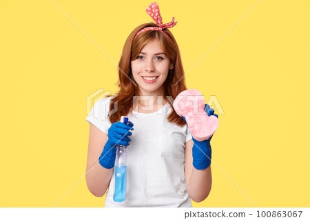Cheerful woman workes of cleaning service holds washing spray and mop, ready to start her work and clean house, satisfied with good chemicals, wears casual domestic clothes, isolated on yellow wall Cheerful woman workes of cleaning service holds washing spray and mop, ready to start her work and clean house, satisfied with good chemicals, wears casual domestic clothes, isolated on yellow wall 100863067