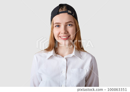 Young beautiful schoolgirl posing in white blouse. Eighteen years old teenage girl looking at camera over bright studio background, being in good mood, has pleasanr expression. Youngster concept. Young beautiful schoolgirl posing in white blouse. Eighteen years old teenage girl looking at camera over bright studio background, being in good mood, has pleasanr expression. Youngster concept. 100863351