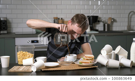 Exhausted man drinking coffee after hard day or night in messy kitchen. Freelance and hardworking concept 100863649