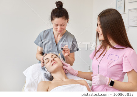 Cosmetologist applying serum essence essential vitamins oils water into face to improve client skin. Beauty expert makes beauty treatment for patient. Health, skin care, aethetic medicine concept. 100863832