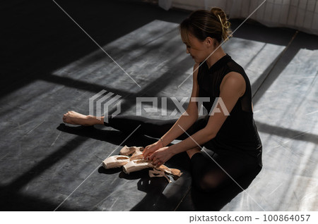 An Asian ballerina sits on the floor and puts on pointe shoes. An Asian ballerina sits on the floor and puts on pointe shoes. 100864057