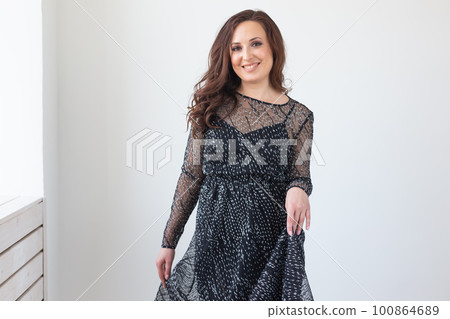 Young pretty lady in black fashion style dress posing in white room, luxury lifestyle people concept Young pretty lady in black fashion style dress posing in white room, luxury lifestyle people concept 100864689