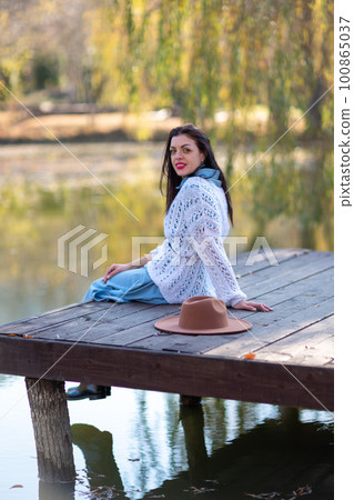 Autumn lake woman. She sits by a pond on a wooden pier in autumn and admires nature. The concept of tourism, weekends outside the city. Autumn lake woman. She sits by a pond on a wooden pier in autumn and admires nature. The concept of tourism, weekends outside the city. 100865037