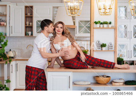 a pregnant woman and a man in pajamas flirt in the kitchen 100865466