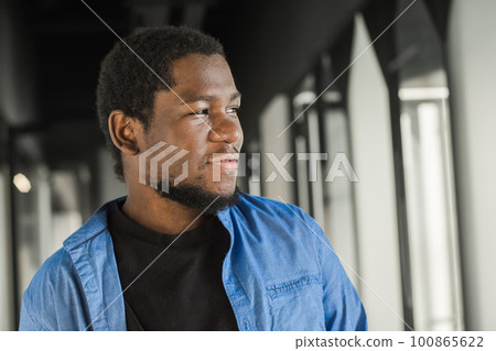 Close-up black serious male face in profile. Man stand with arms folded. Portrait of pensive african american man looking out window in office thinking making decision turns head to camera Close-up black serious male face in profile. Man stand with arms folded. Portrait of pensive african american man looking out window in office thinking making decision turns head to camera 100865622