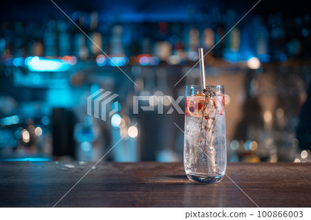modern gin tonic cocktail with ice, straw and red berries on bar counter modern gin tonic cocktail with ice, straw and red berries on bar counter 100866003