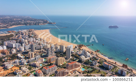 Aerial view of Portuguese city of Portimao with buildings on coast with beaches. Tourist cruise liner in the background in the sea. Aerial view of Portuguese city of Portimao with buildings on coast with beaches. Tourist cruise liner in the background in the sea. 100866251