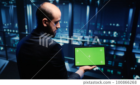 Professional server engineer using greenscreen on tablet, inspecting cloud computing in data center. Support specialist looking at blank copyspace and chroma key template. Tripod shot. 100866268