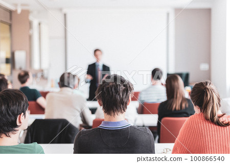 Speaker giving presentation in lecture hall at university. Participants listening to lecture and making notes. Copy space for brand on white screen. Speaker giving presentation in lecture hall at university. Participants listening to lecture and making notes. Copy space for brand on white screen. 100866540