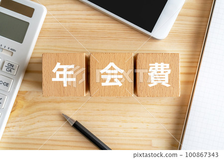 A block with the annual fee written on it, a calculator, a smartphone, a notebook, and a pen 100867343