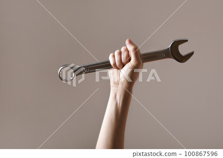 big spanner in the woman's hand. hand holds a wrench on a gray background. Combination wrench. big chrome vanadium spanner in the hand. women's work. labor day. big spanner in the woman's hand. hand holds a wrench on a gray background. Combination wrench. big chrome vanadium spanner in the hand. women's work. labor day. 100867596