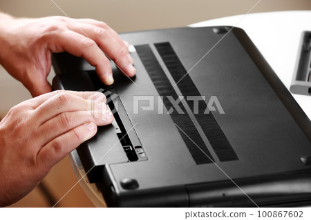 Repairman's hands removing the power battery from the laptop. Computer service and repair concept. Laptop disassembling in repair shop. Electronic development, electronic device fixing. 100867602