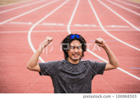 Male runner doing fist pump on athletics track 100868503