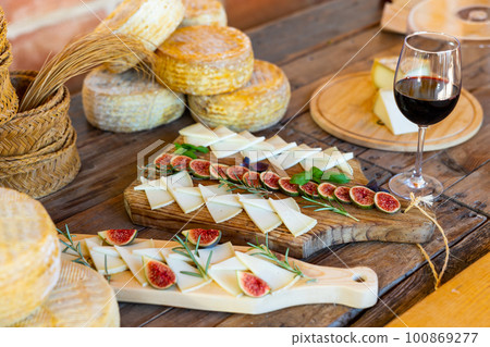 Slices of delicious cheese served with glass of red wine on wooden table in winery Slices of delicious cheese served with glass of red wine on wooden table in winery 100869277