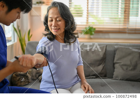 Happy retired Asian woman is being checked for blood pressure with an electric monitor 100872498