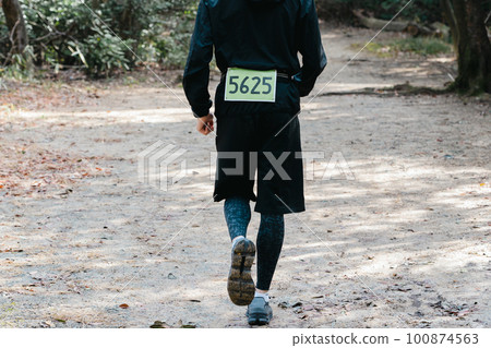 Rear view of a male runner wearing a bib on a trail run 100874563