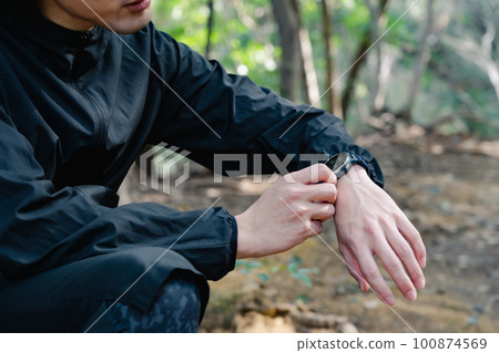 Male runner checking smartwatch in forest 100874569