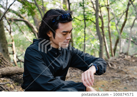 Male runner looking at smartwatch in forest 100874571