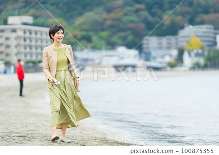 拿著相機在沙灘上散步的中年婦女 100875355