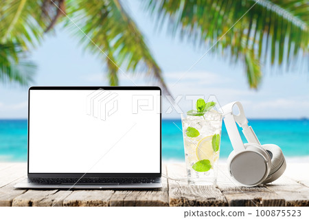 Laptop and headphones on wooden table in front of sunny sea Laptop and headphones on wooden table in front of sunny sea 100875523