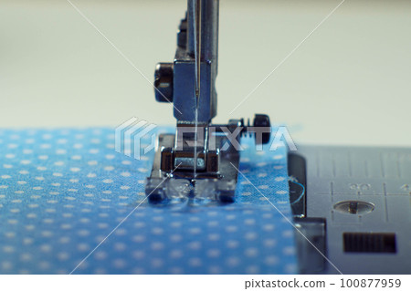Detailed close up shot of sewing machine steel foot with needle and thread stitching on blue fabric polka dot textile Detailed close up shot of sewing machine steel foot with needle and thread stitching on blue fabric polka dot textile 100877959
