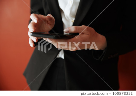 Young adult woman using smartphone next to the red wall Young adult woman using smartphone next to the red wall 100878331