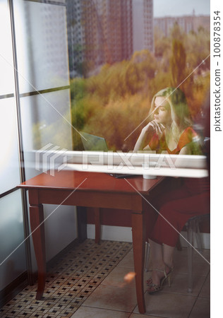 Young adult woman sitting at the table and working on laptop 100878354