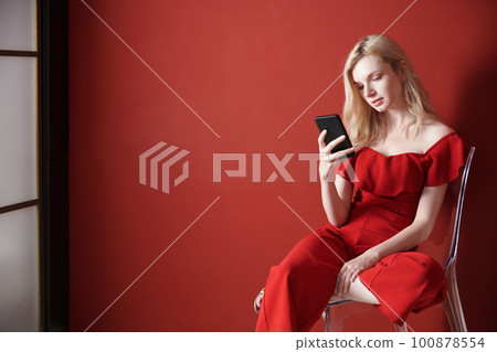 Young adult woman relaxing on a chair and using smartphone 100878554