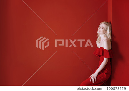 Beautiful young adult woman wearing red jumpsuit standing next to the wall Beautiful young adult woman wearing red jumpsuit standing next to the wall 100878559