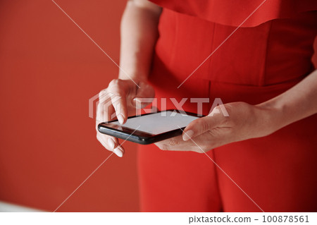 Young adult woman using smartphone next to the red wall 100878561