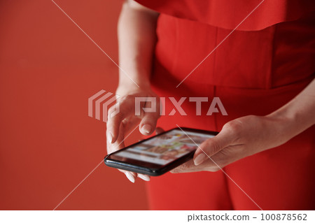 Young adult woman using smartphone next to the red wall 100878562
