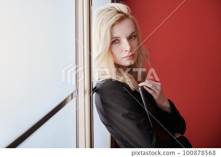 Young adult business woman standing next to the window holding laptop 100878568